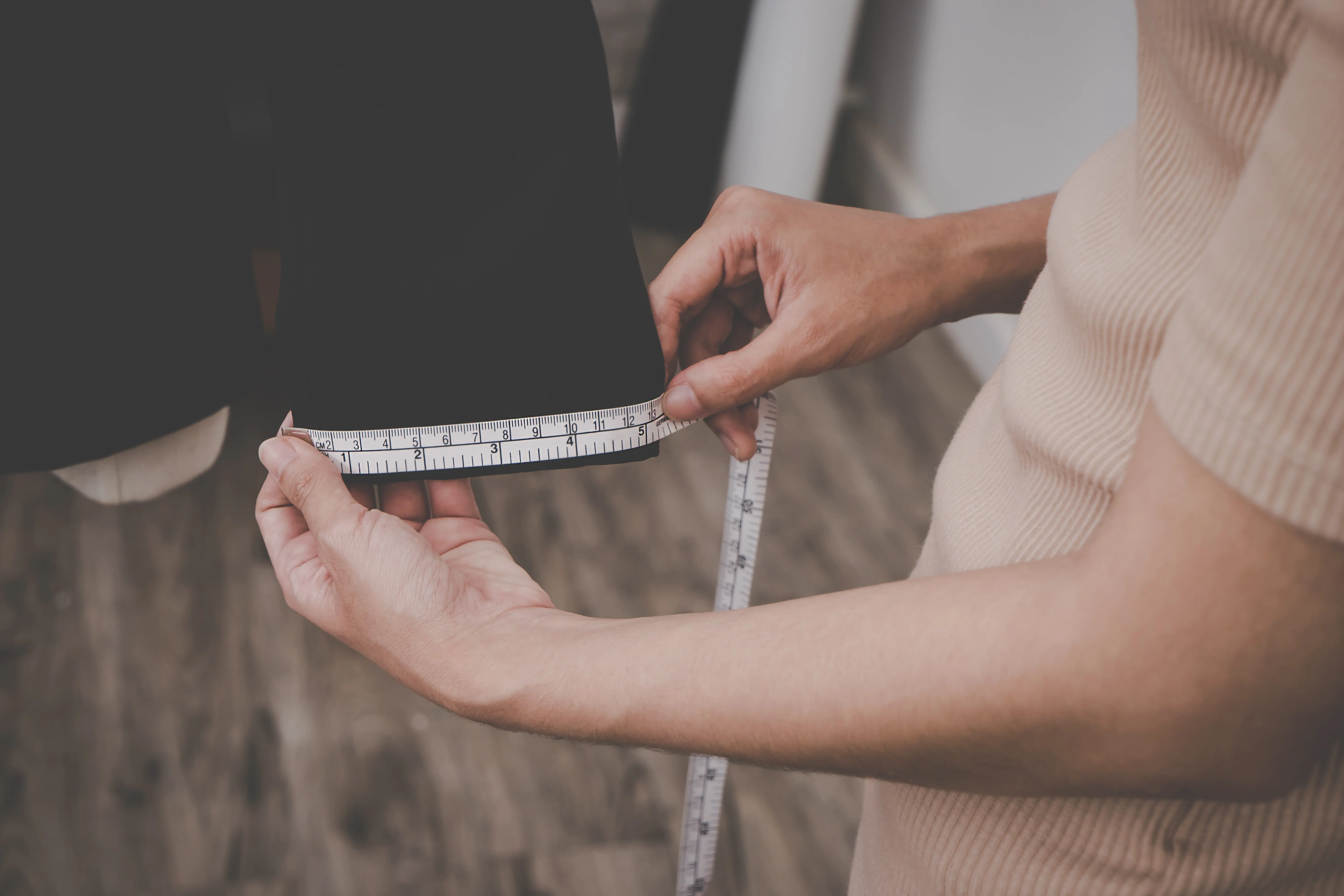 Eine Schneiderin misst eine Jacke mit einem Maßband.