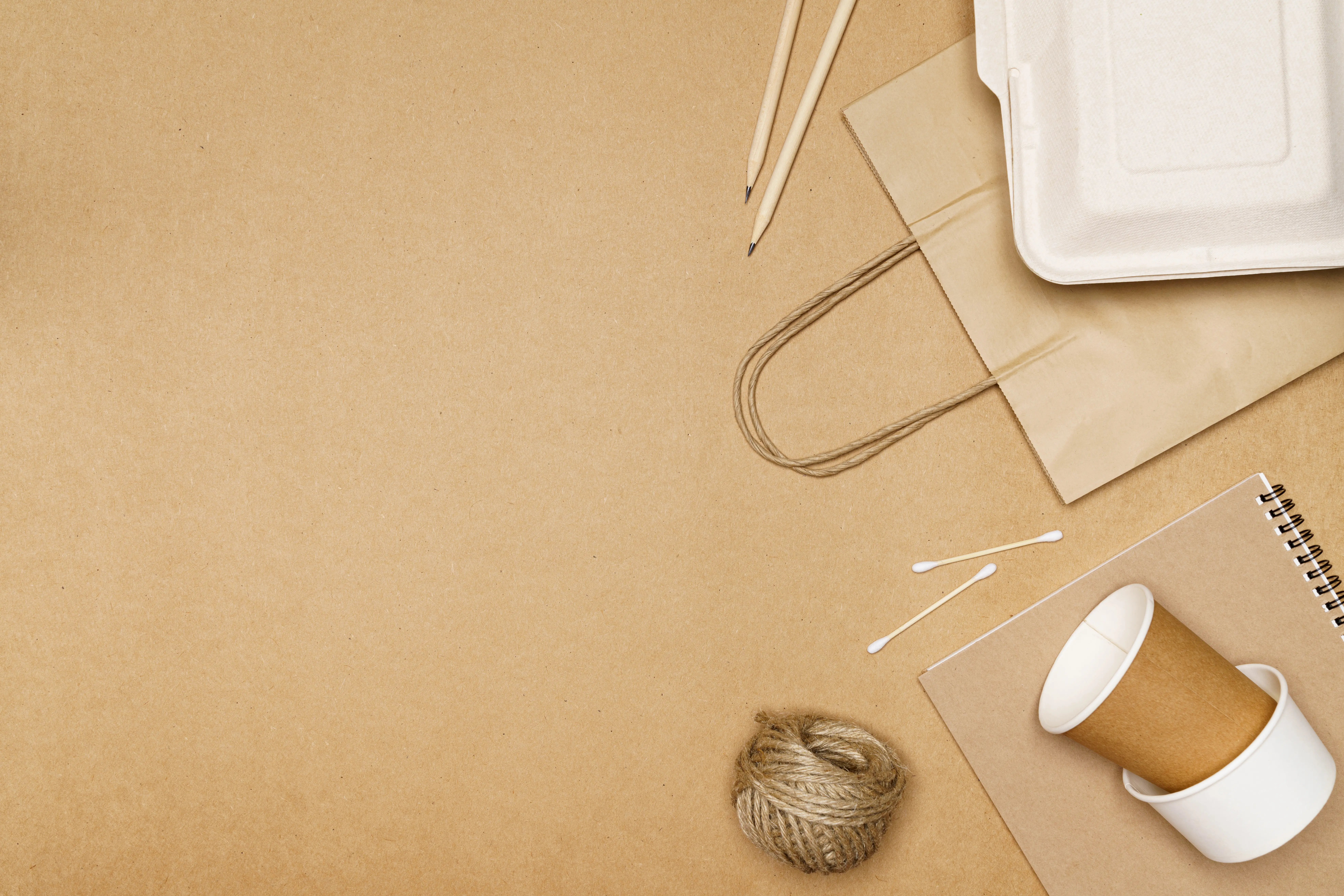 Umweltfreundliches Konzept mit Lieferessenbehälter auf einer Papiertüte sowie Notizbuch und Bleistift mit Juteschnur.